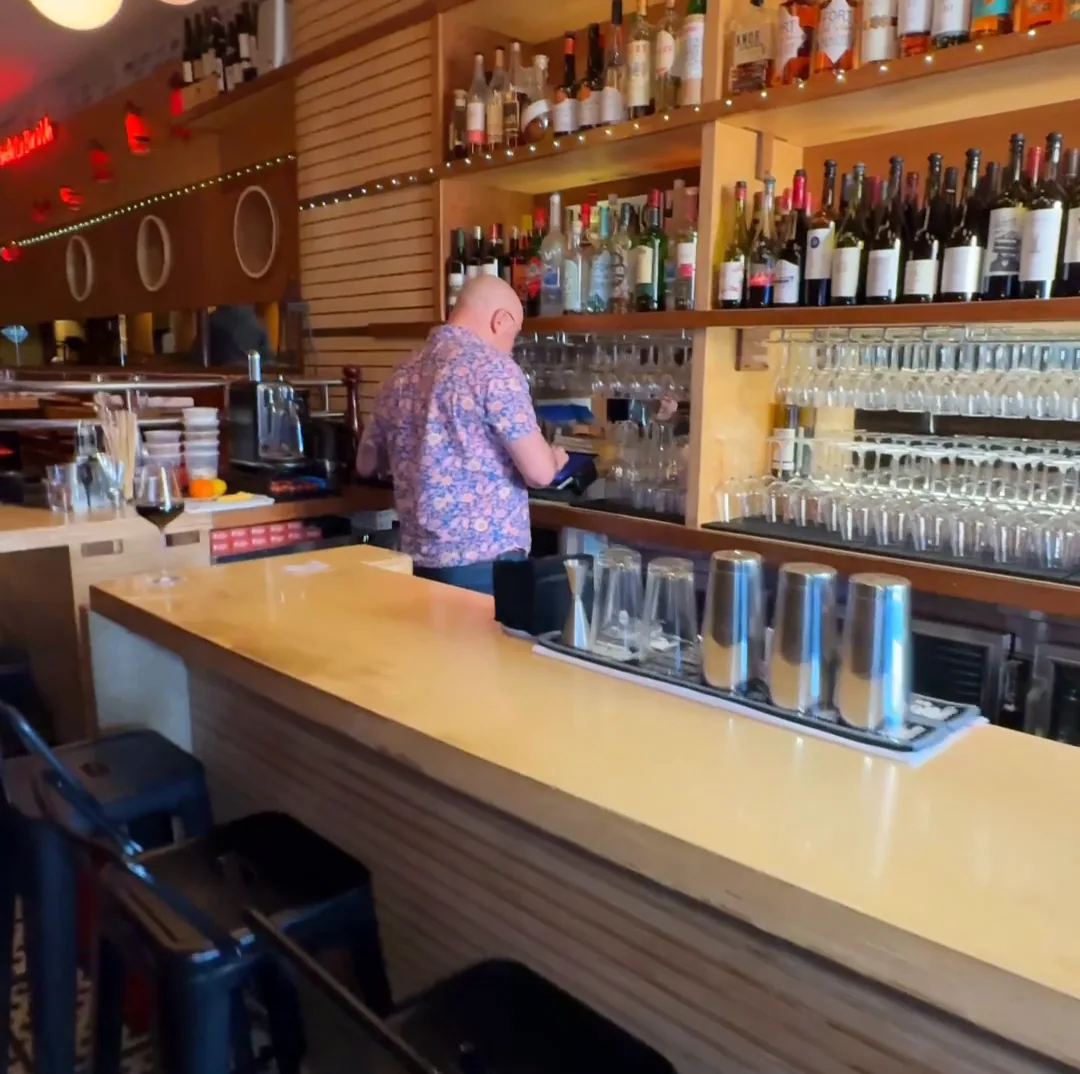 The long blond bar at Amélie Upper West Side running the length of the room past shelves of wine