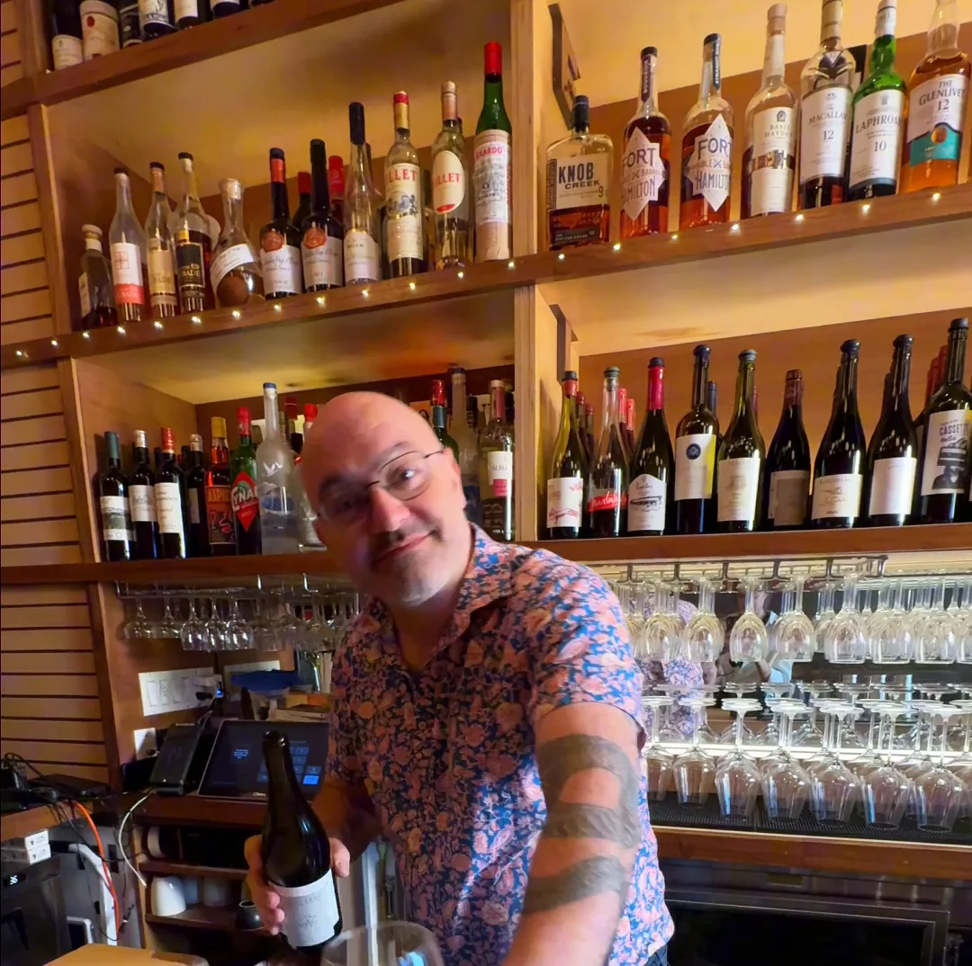 Amélie's sommelier behind the Upper West Side bar setting down a glass beside an open bottle of red