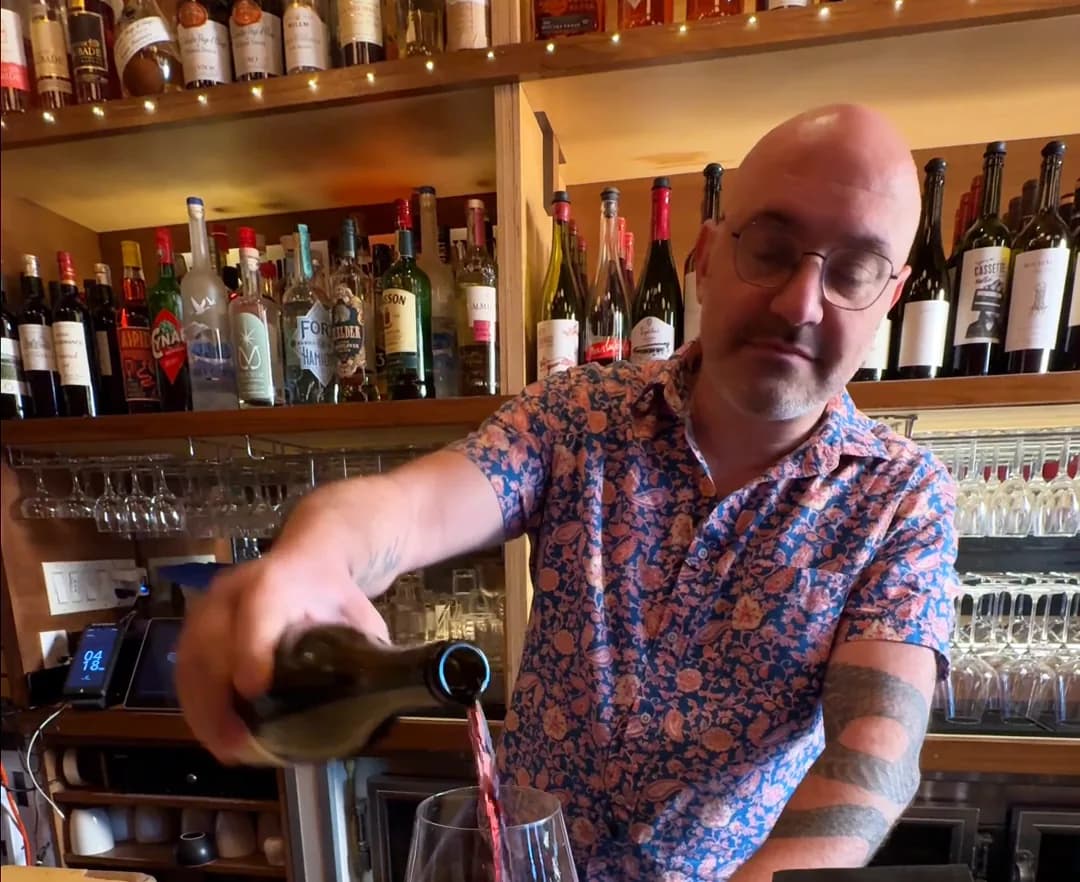 Red wine being poured into a glass on the blond bar top at Amélie Upper West Side