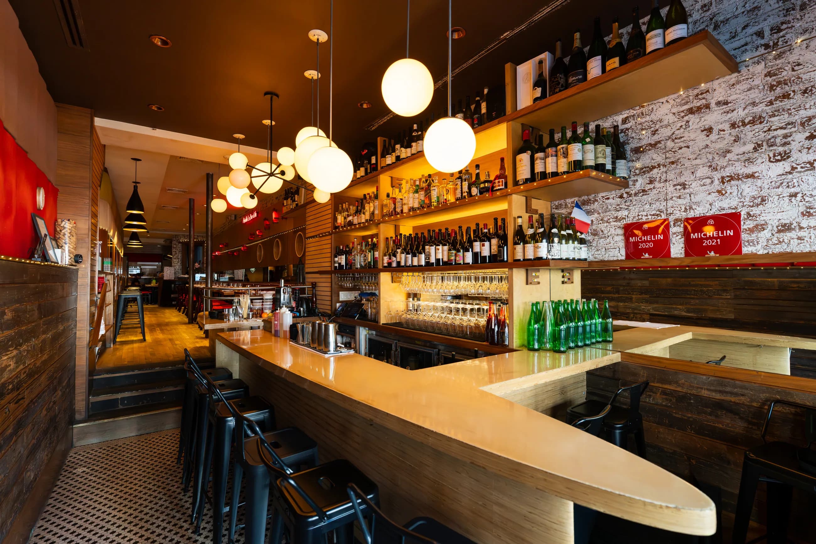 The bar at Amélie Upper West Side, globe lights over a whitewashed brick wall lined with bottles