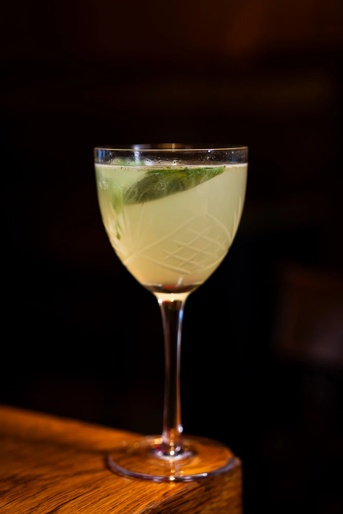 A pale green cocktail with mint in a wine glass on the bar at Amélie Upper West Side