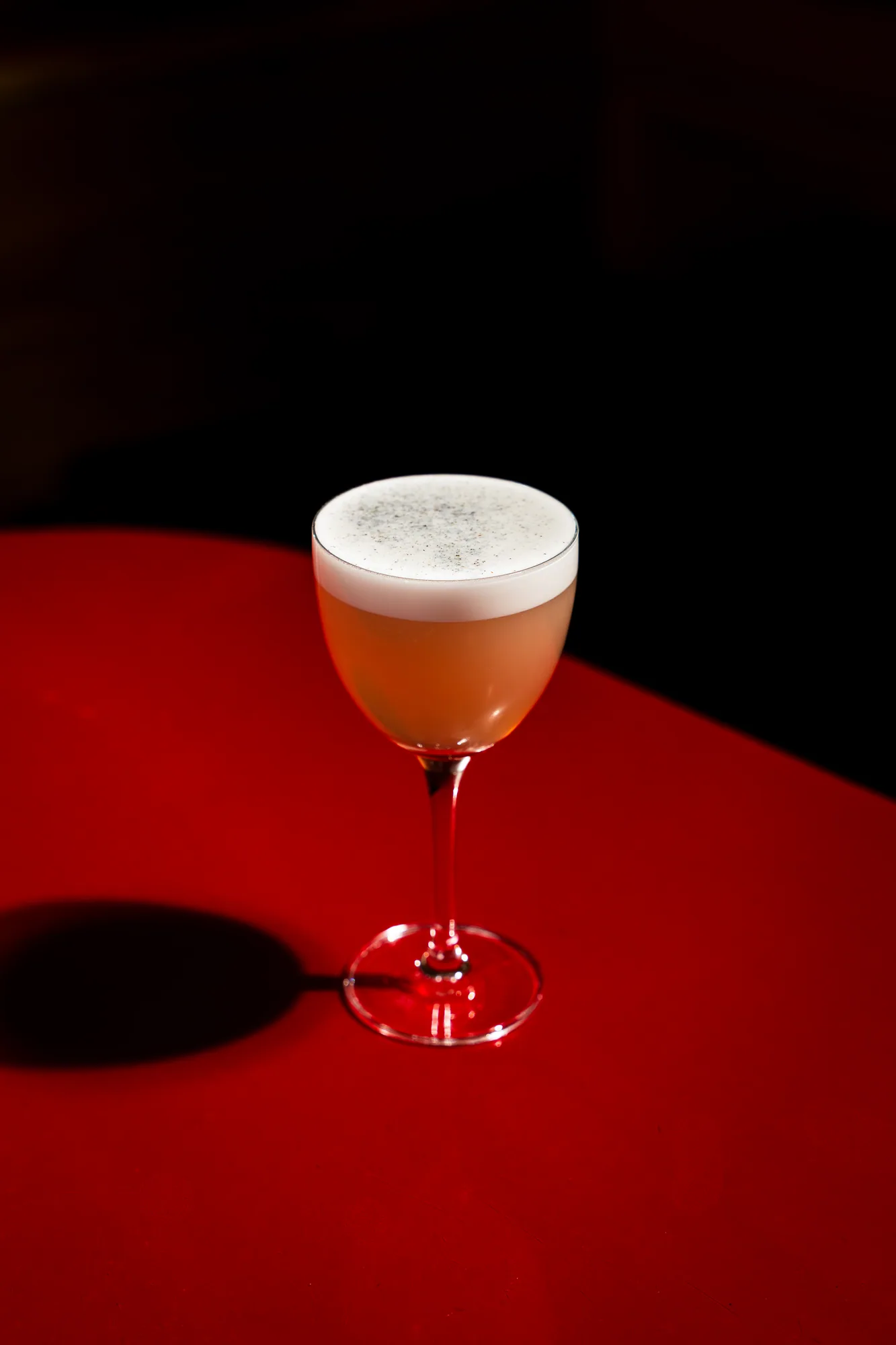 A cocktail with a thick foam top standing on the red bar at Amélie Upper West Side