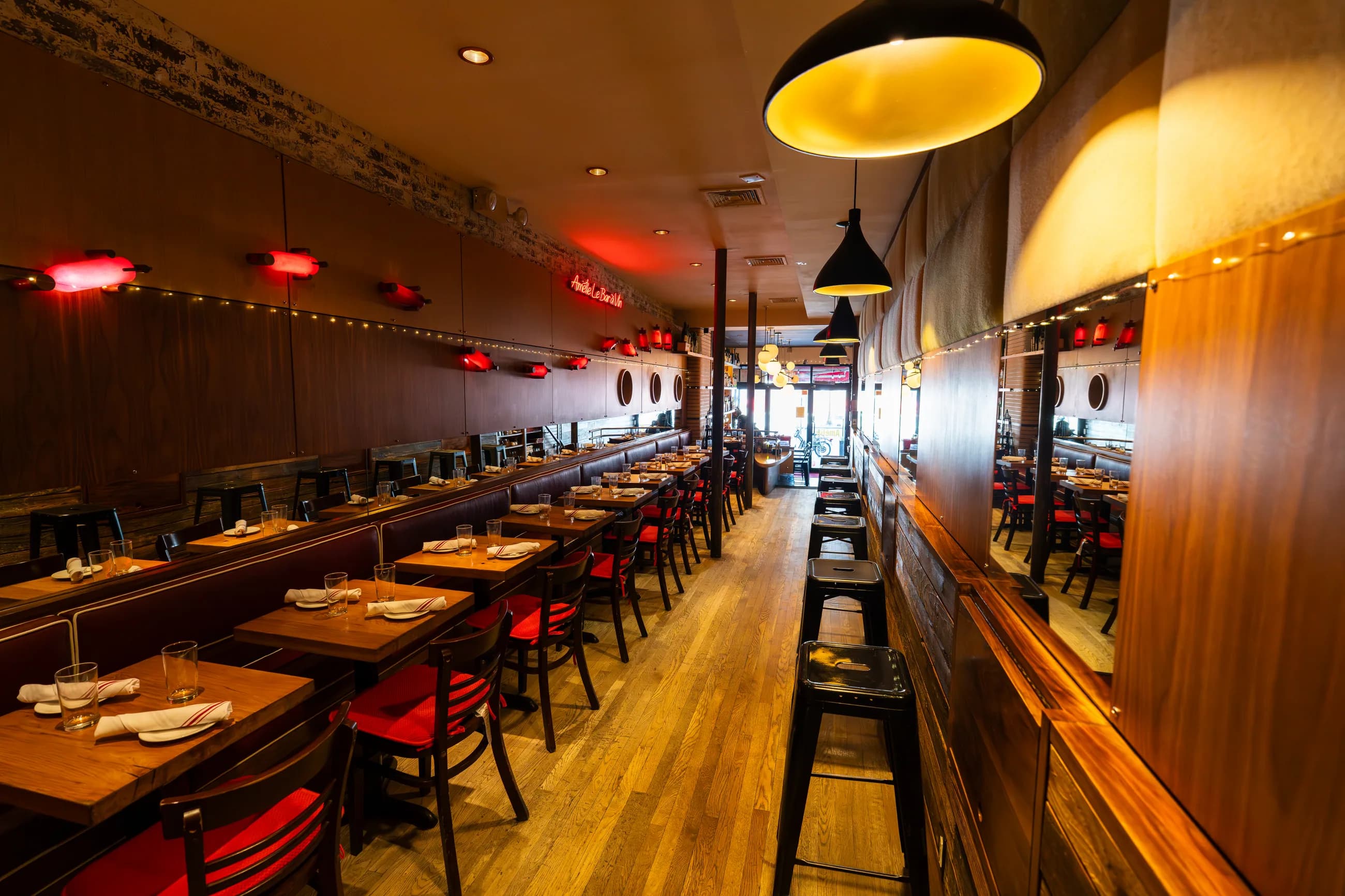 A wide view of the dining room at Amélie Upper West Side, warm wood and red accents under low pendant light