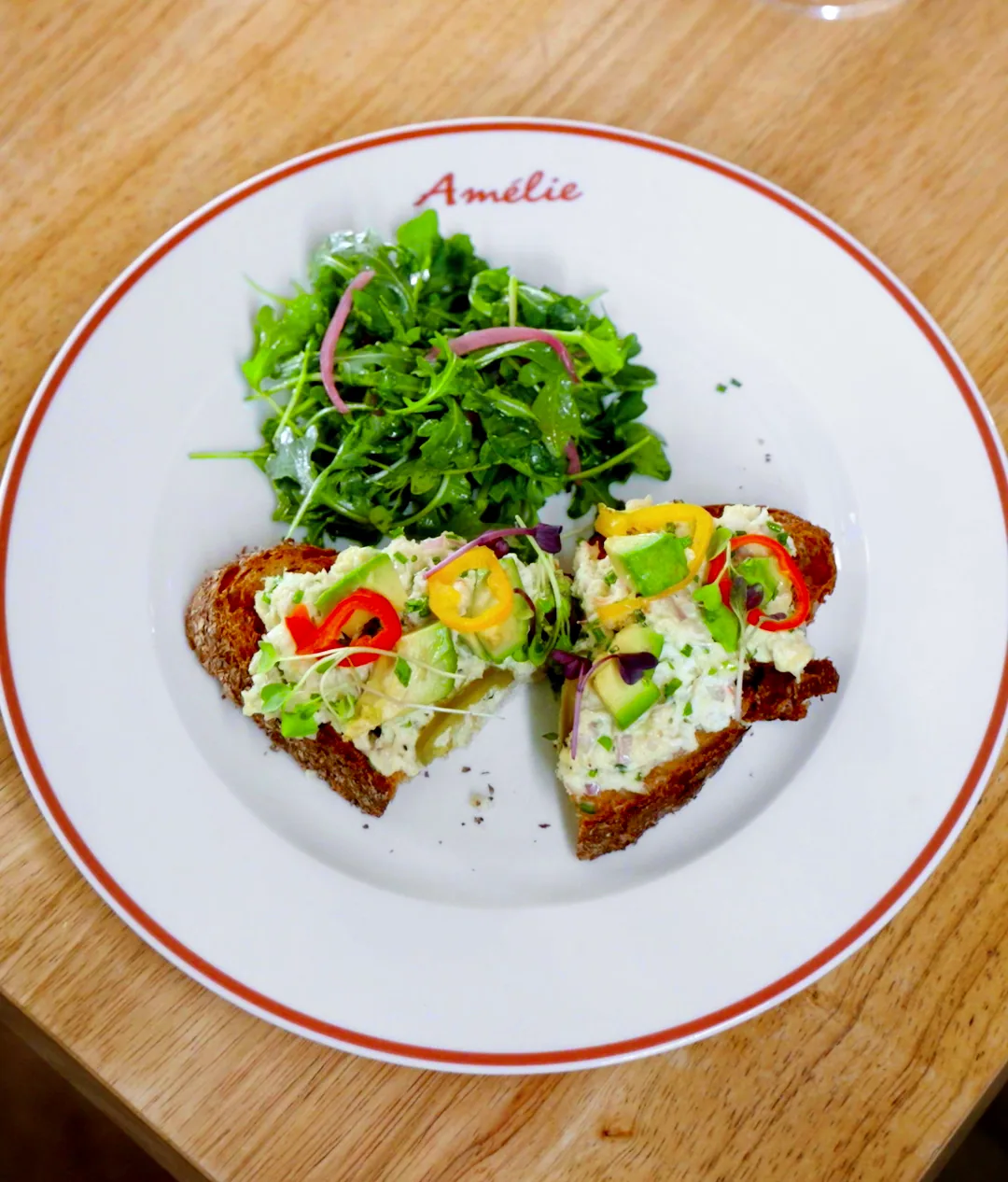 Crab tartine on toasted sourdough with peppers and a tangle of arugula, on an Amélie red-rimmed plate