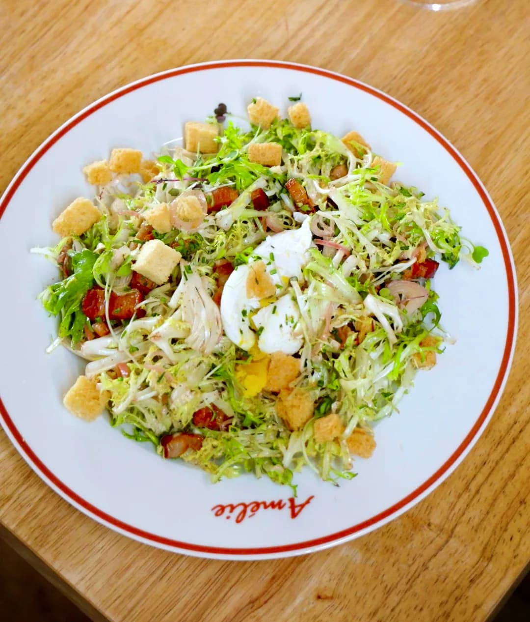 Salade lyonnaise of frisée, lardons and croutons under a poached egg on an Amélie red-rimmed plate