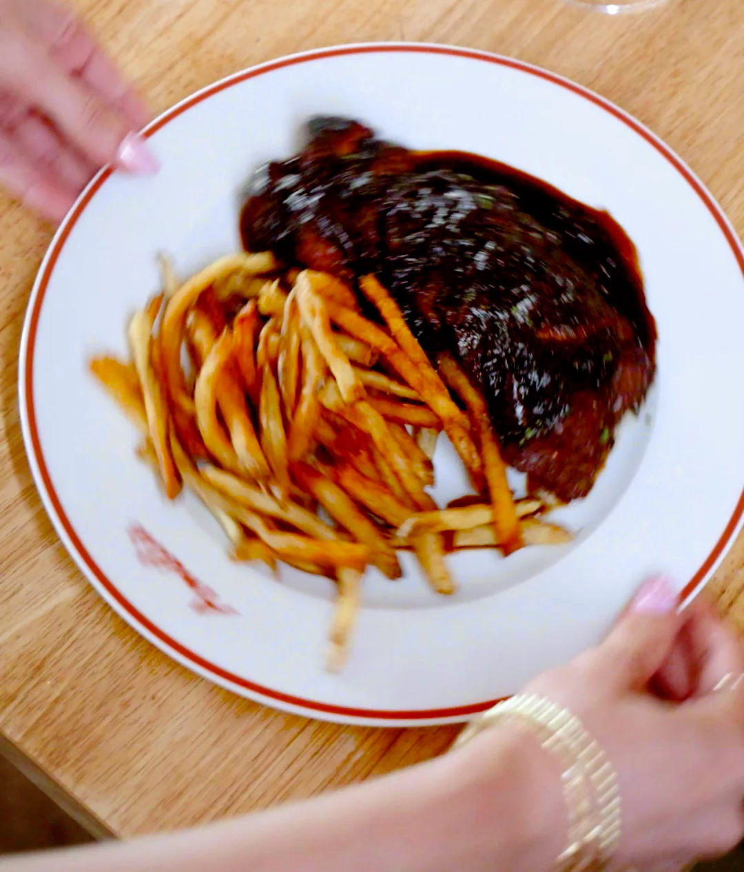 Steak frites in red wine sauce with a nest of thin fries on an Amélie red-rimmed plate, shot from above
