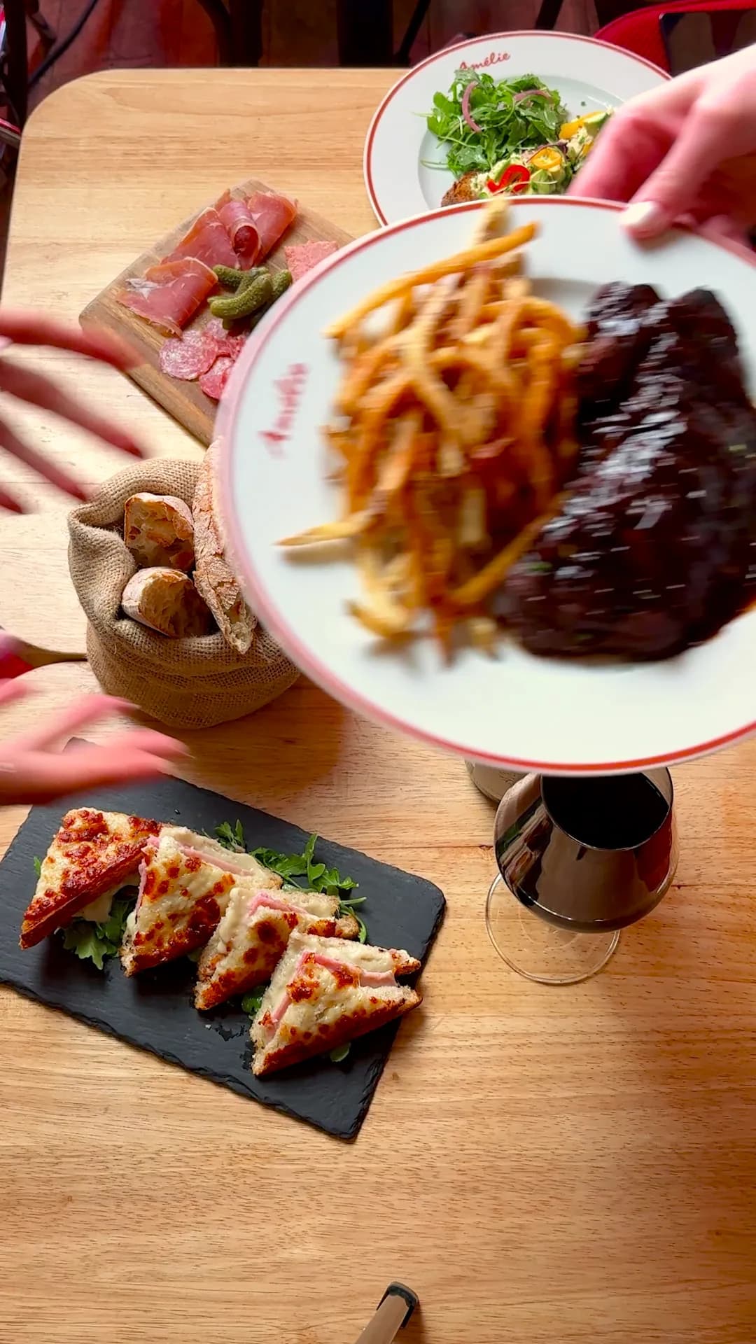 A wooden table seen from above with a charcuterie board, croque monsieur bites on slate, a tartine and steak frites