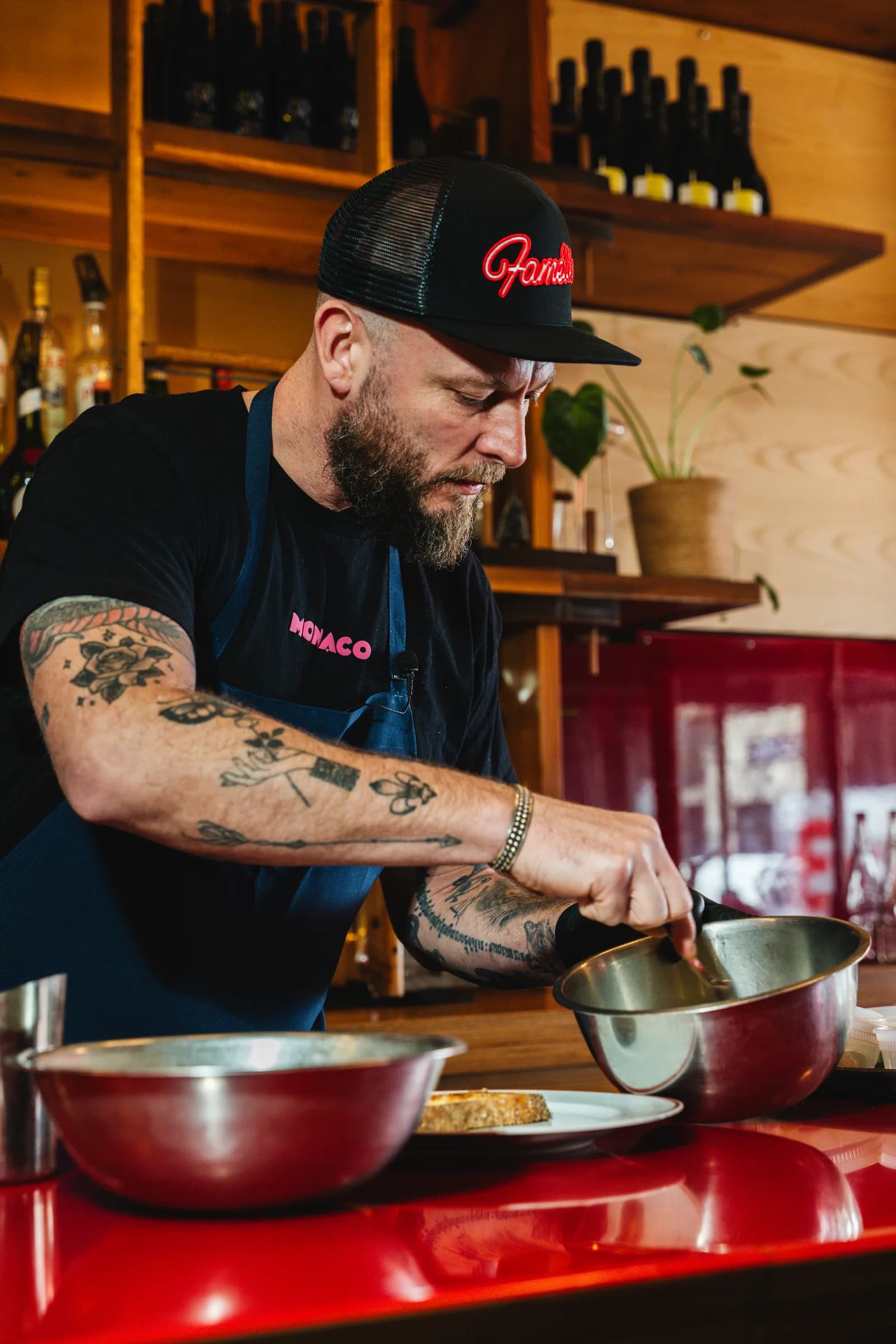 A chef working over steel bowls at the pass at Amélie West Village, shelves of bottles behind