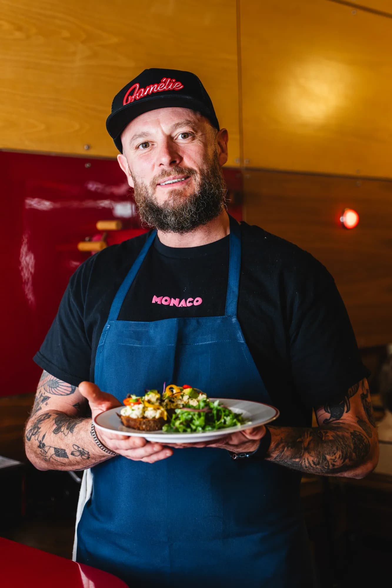 A chef at Amélie West Village holding a finished plate in front of the red bar