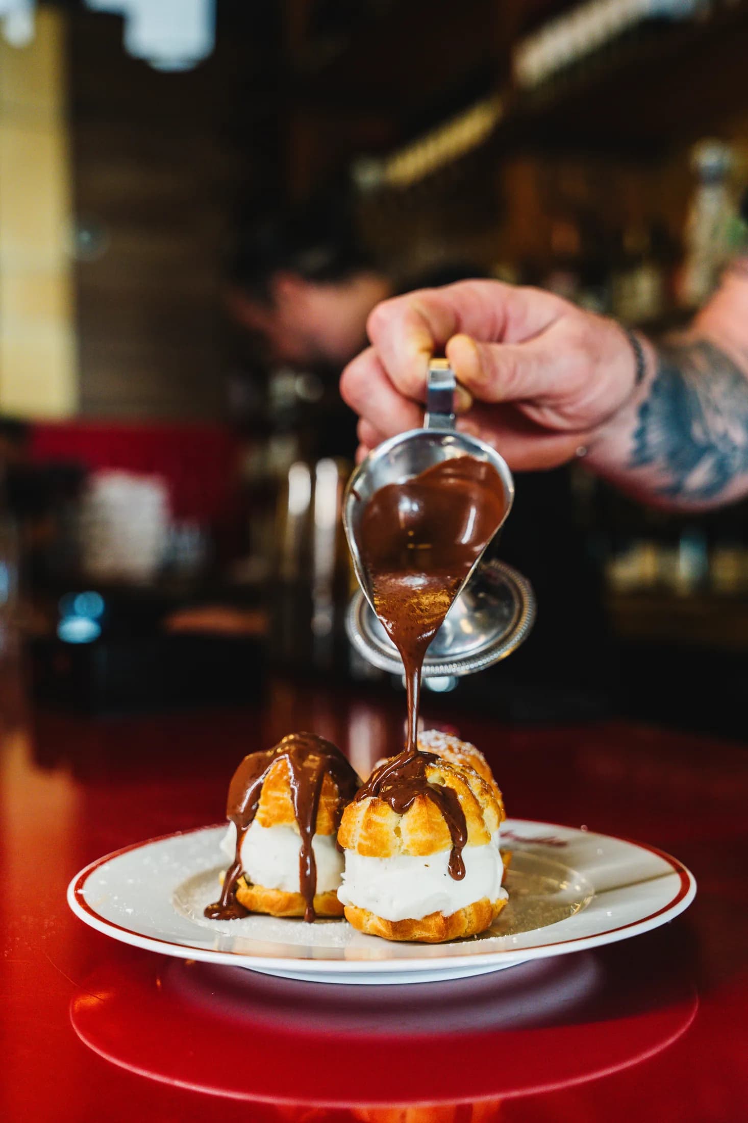Warm chocolate being poured over profiteroles on a plate at Amélie West Village